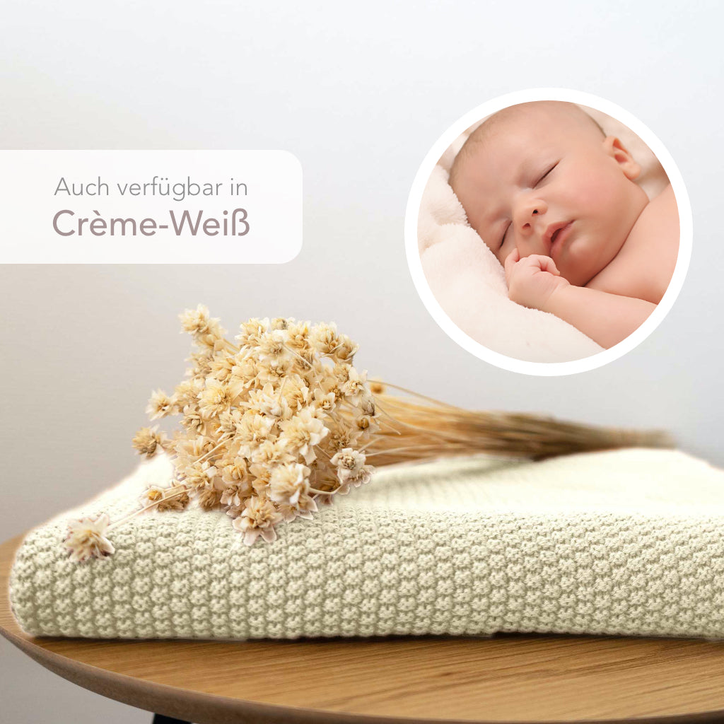 Strickdecke von Kinderzimmer.de in creme-weiss, dargestellt mit schlafendem Baby